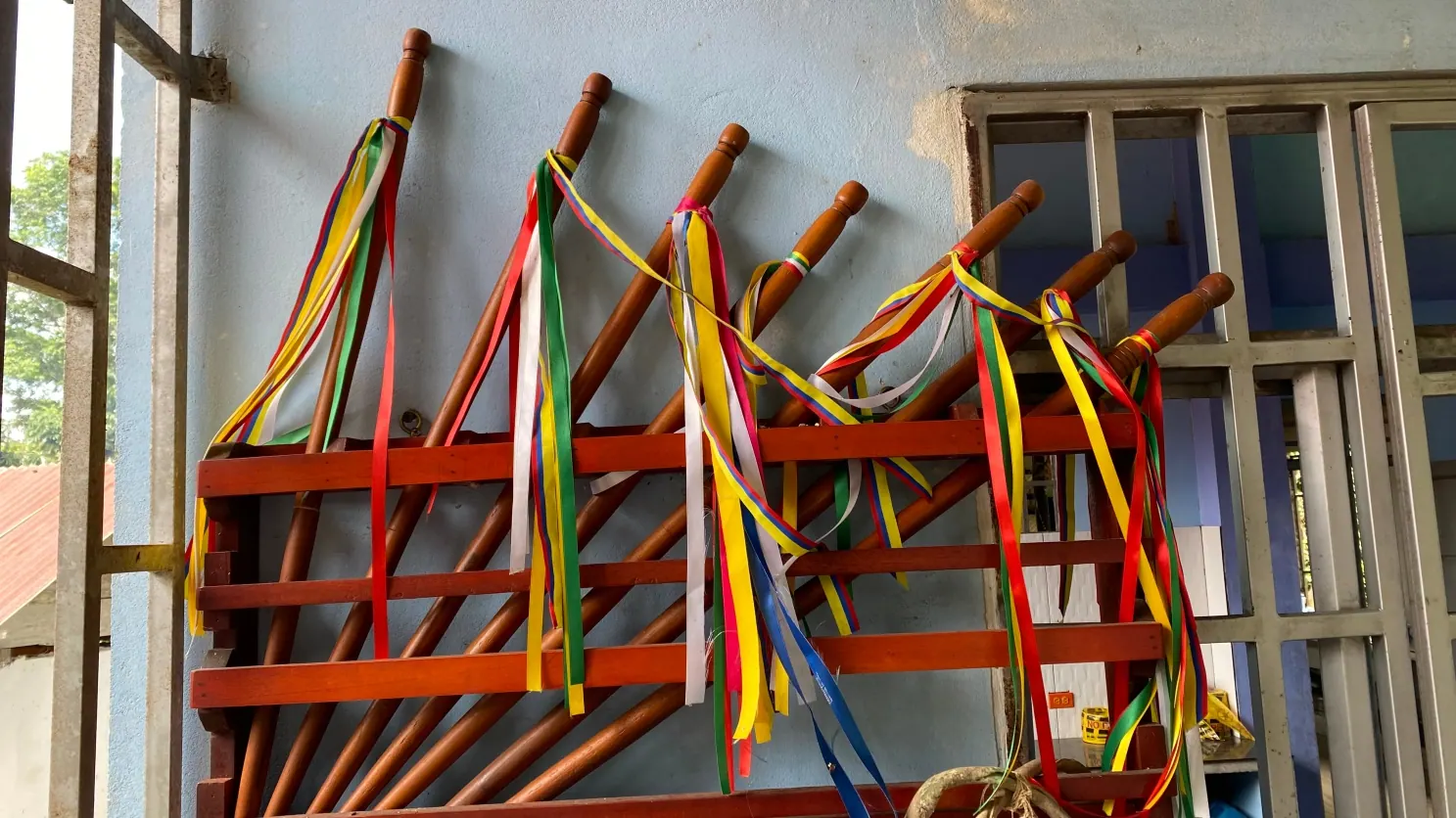 Bastones de mando con cintas de colores colgados en un soporte rojo junto a una ventana.