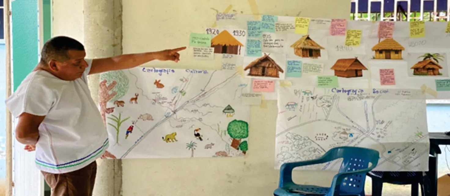 Hombre señalando una cartografía social pegada en la pared, con dibujos de casas y notas.
