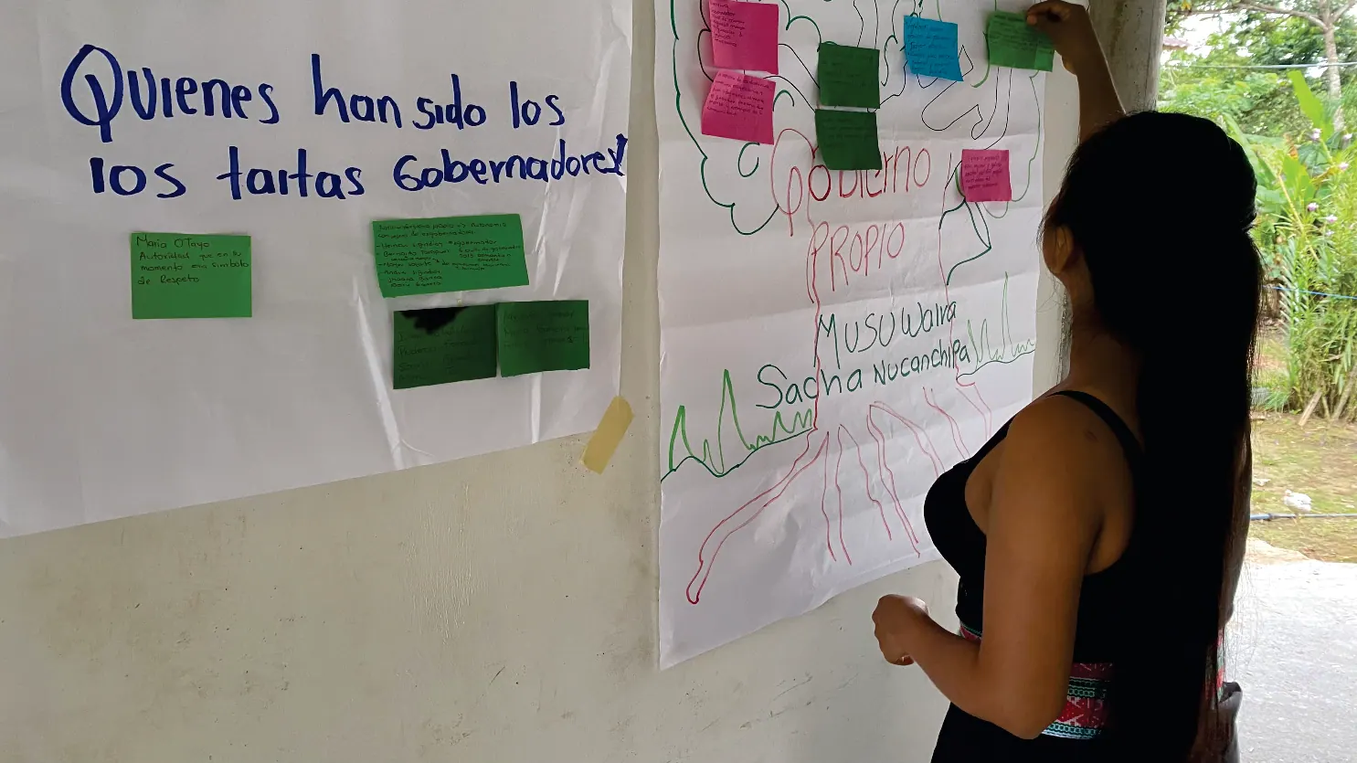 Mujer pegando notas en una cartelera titulada «¿Quiénes han sido los taitas gobernadores?».