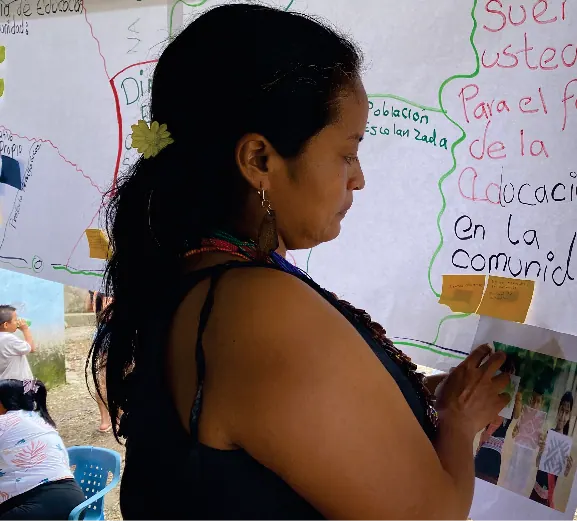 Mujer con traje tradicional leyendo frente a una cartelera de educación.