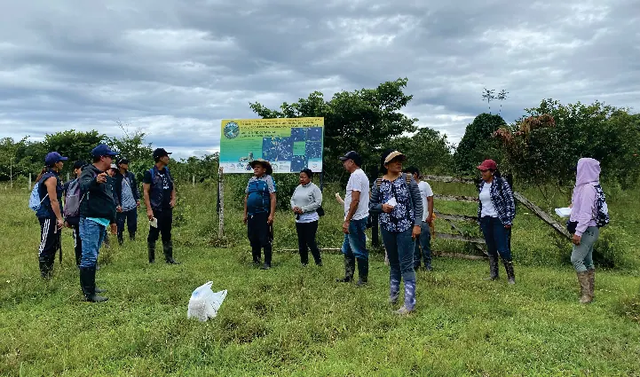Grupo de personas de pie en un campo abierto con un aviso al fondo.
