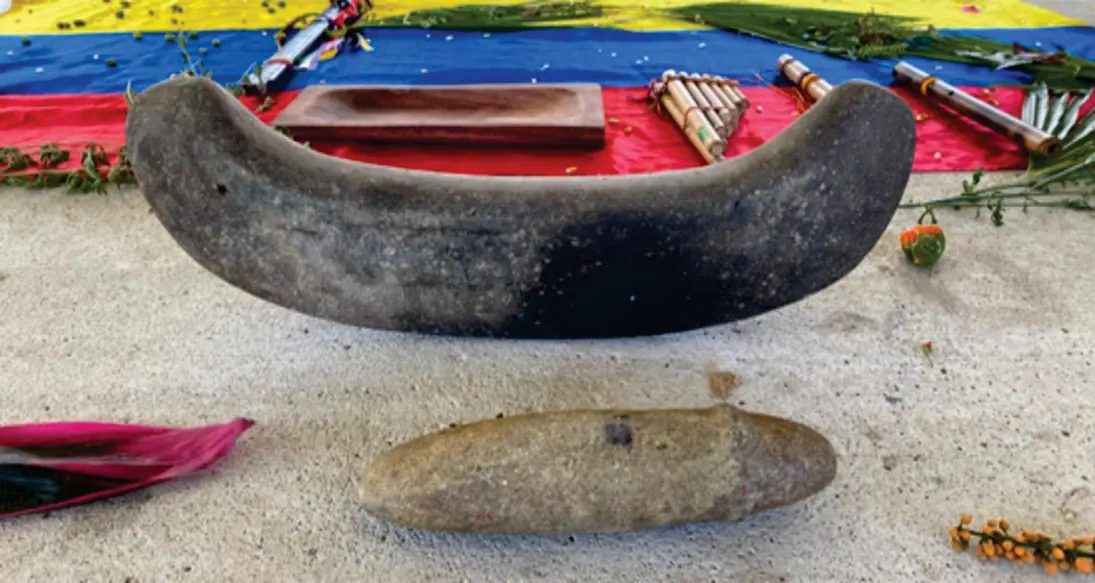 Batea de madera y piedra de moler sobre una bandera, con tejidos alrededor.
