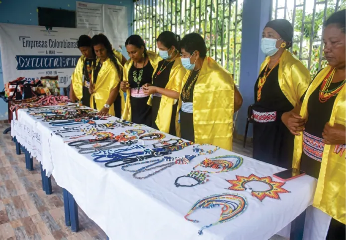 Mujeres con chalinas amarillas exhibiendo artesanías de chaquira sobre una mesa.