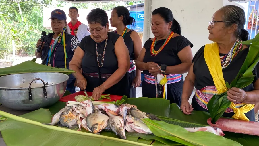 Mujeres con traje tradicional preparando pescado sobre hojas de plátano.