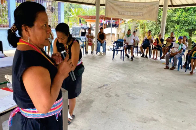 Mujer con traje tradicional hablando con micrófono en una reunión.