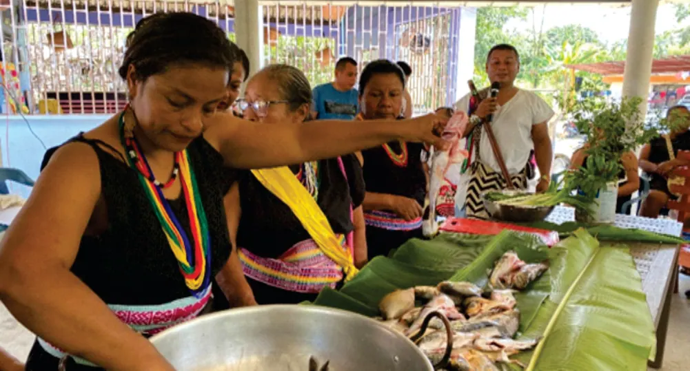 Mujeres cocinando pescado en una olla sobre hojas de plátano.