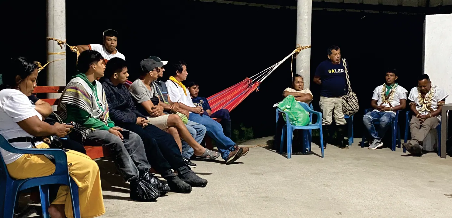 Reunión bajo techo con una hamaca colgada y personas sentadas.