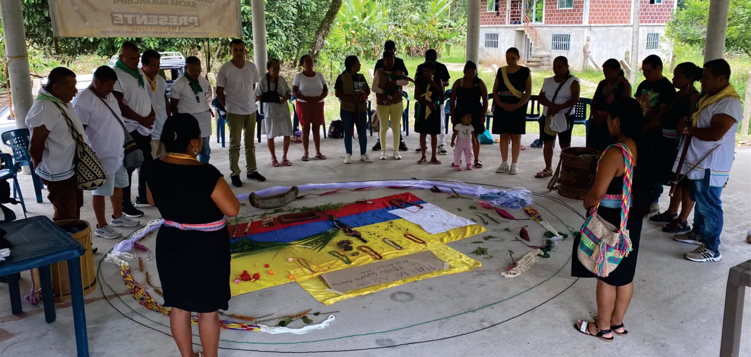 Asamblea en círculo con banderas y tejidos extendidos en el suelo.