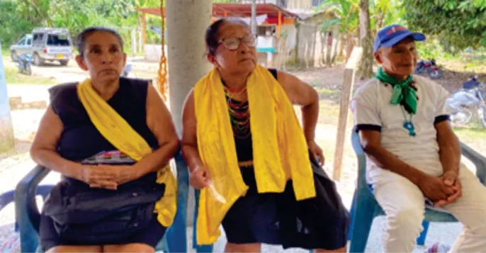 Dos mujeres mayores con chalinas amarillas y un hombre sentados.