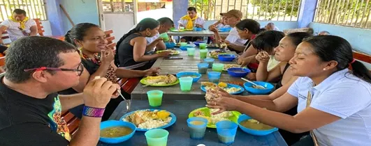 Personas compartiendo alimentos en una mesa larga.