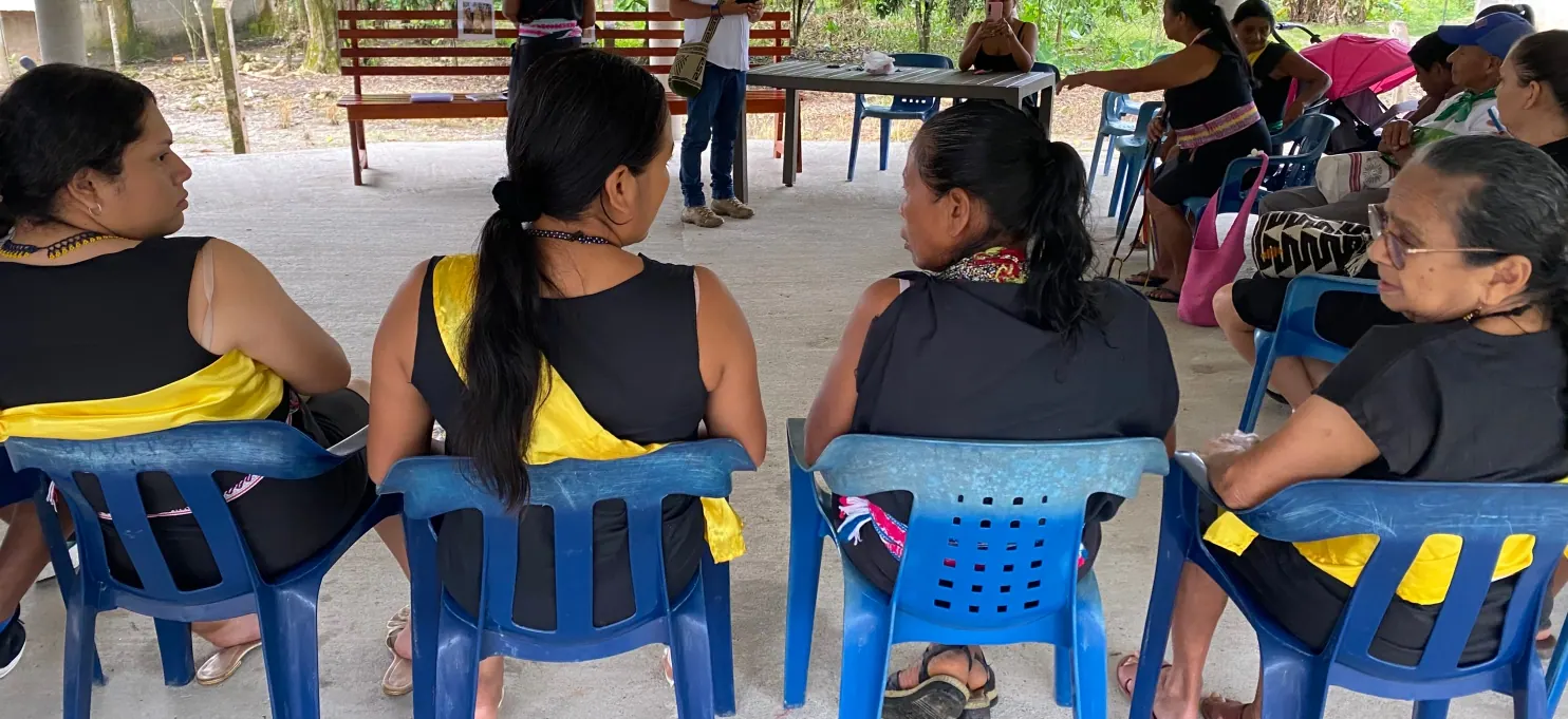Mujeres con traje tradicional sentadas de espaldas en sillas azules.