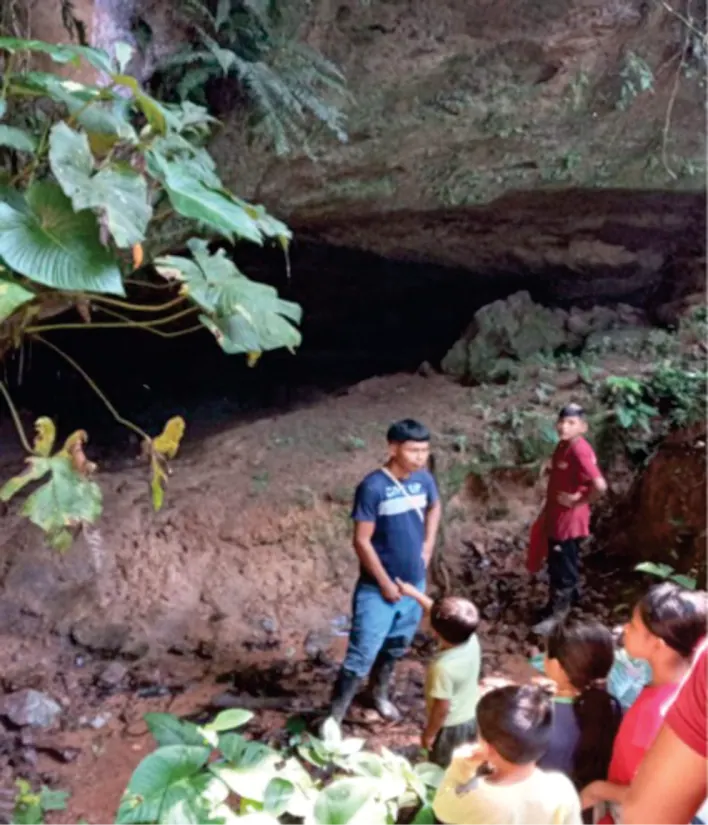 Personas, entre ellas niños, en la entrada de una cueva rodeada de vegetación.
