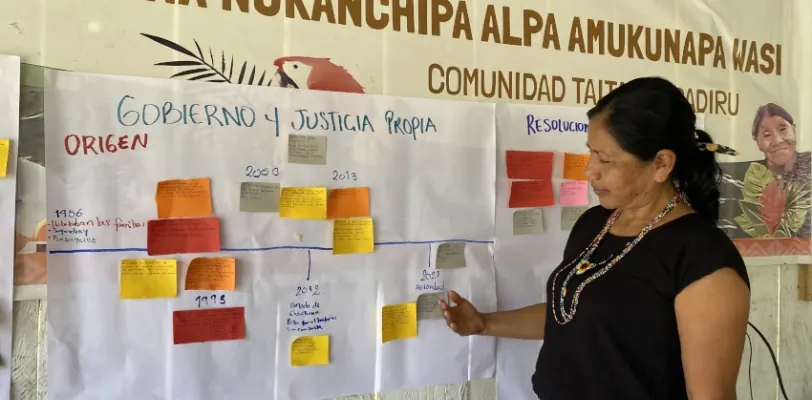 Mujer frente a una cartelera de «Gobierno y Justicia Propia» con línea de tiempo.