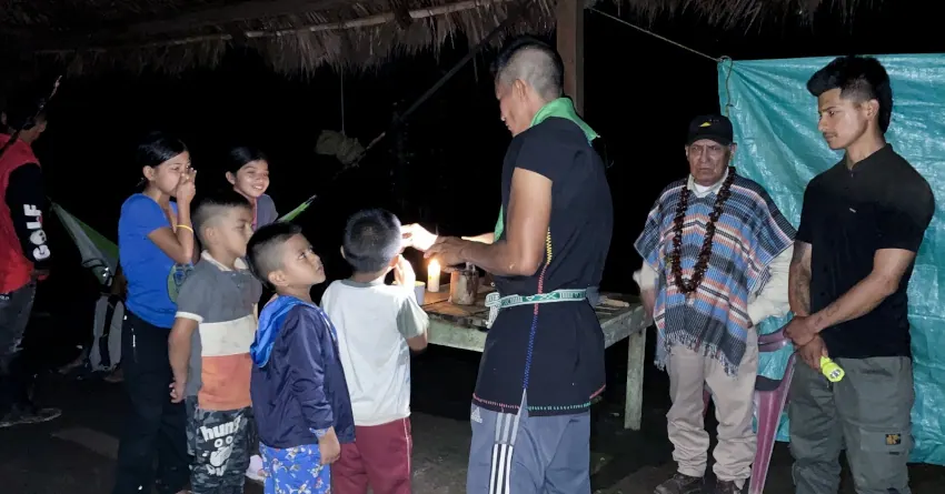 Reunión nocturna con niños y adultos de pie alrededor de una mesa.