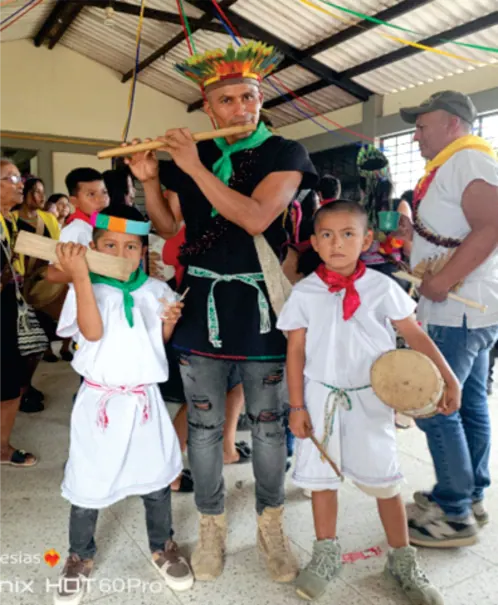 Músico con corona de plumas tocando flauta junto a niños con traje tradicional.