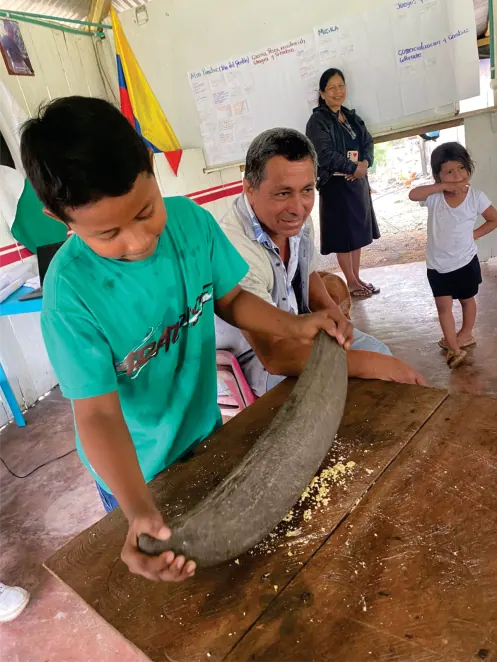Niño moliendo maíz en una batea de madera.