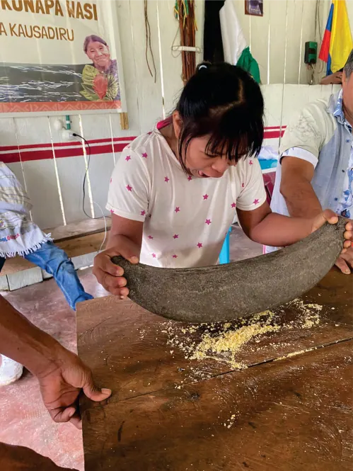 Niña moliendo maíz en una batea de madera.