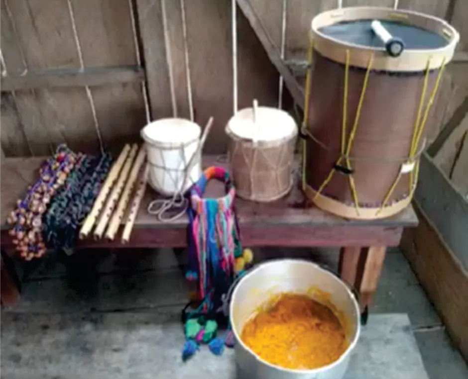 Instrumentos tradicionales (tambor, flautas) y una olla con alimento en un espacio de madera.