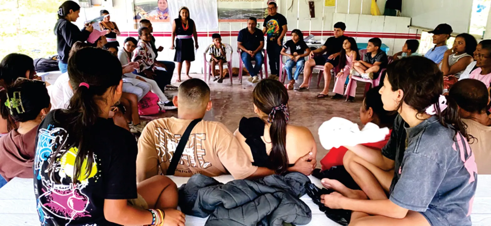 Taller con niños y adultos sentados en el piso de un salón.