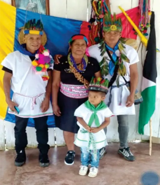 Familia con traje tradicional y coronas frente a una bandera; un niño al frente.