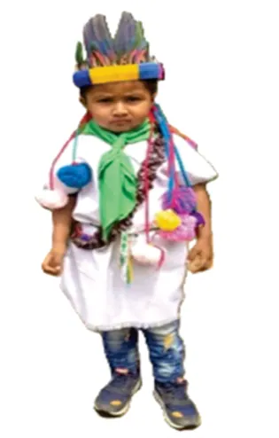 Niño con traje tradicional blanco, pañoleta verde y corona de plumas, sobre fondo blanco.