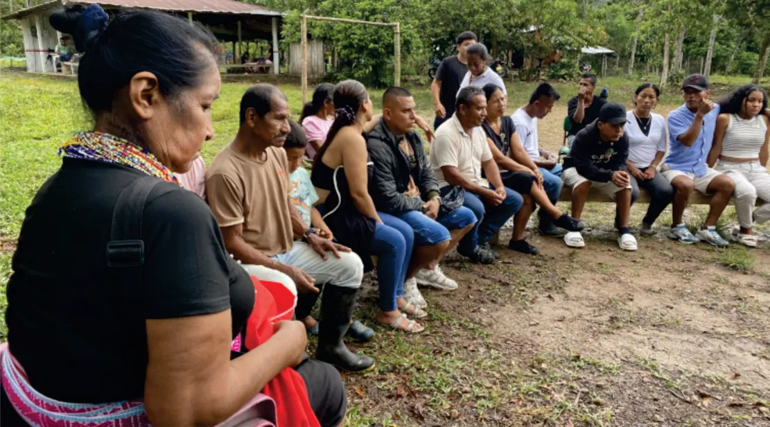 Mujer y grupo de personas sentados en una banca al aire libre.
